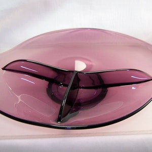 May include: A purple glass serving dish with three divided sections. The dish has a wavy, organic shape.