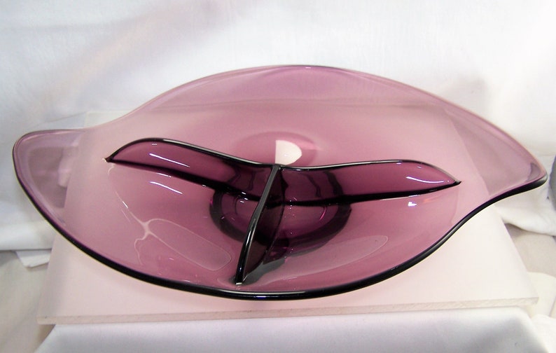 May include: A purple glass serving dish with three divided sections. The dish has a wavy, organic shape.