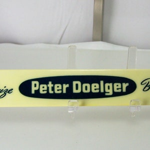 May include: A yellow plastic sign with black lettering that reads "First Prize Peter Doelger Beer and Ale".