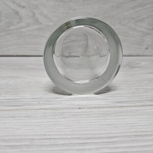 以下が含まれることがあります： 厚い丸いベースを持つ、下から見た透明なガラスのタンブラー。 ガラスの縁の周りはすりガラスのように見え、中央は滑らかで透明です。 背景は明るい灰色の木製の表面です。