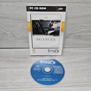 May include: A PC CD-ROM game case and disc for "Hitman: Codename 47." The case shows a man in a suit holding a gun. The disc is blue with white text, and the game title is printed on both the case and the disc.
