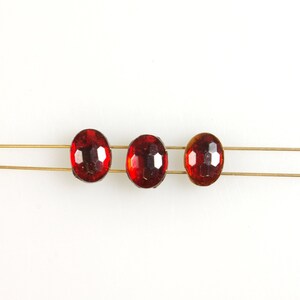 May include: Three red oval-shaped rhinestones are strung on a thin gold wire.