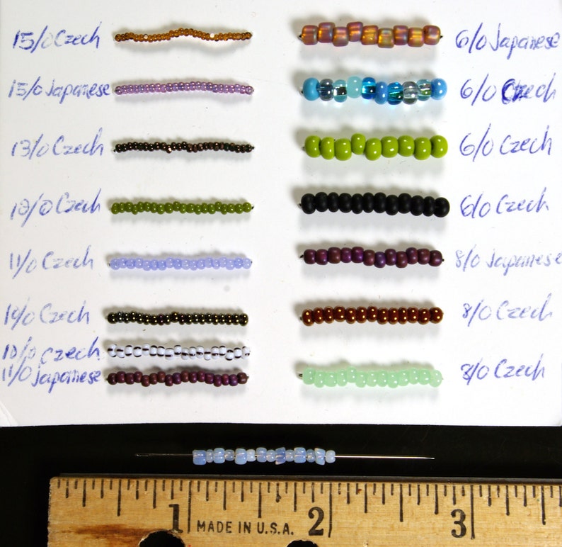 May include: A close-up of a white card with rows of different colored beads labeled with their size and type. The beads are arranged in rows, with the largest beads at the top and the smallest beads at the bottom. The card is labeled with the bead size and type, such as "15/0 Czech" and "6/0 Japanese".
