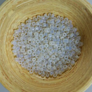 May include: A bowl filled with white iridescent glass seed beads. The beads are small and round, with a slight shimmer.
