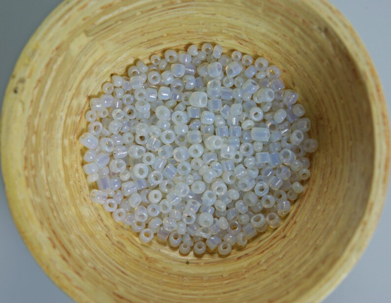 May include: A bowl filled with white iridescent glass seed beads. The beads are small and round, with a slight shimmer.