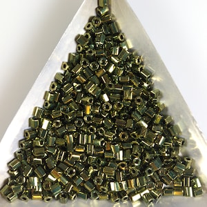 May include: A close-up of a pile of small, gold-toned, cylindrical beads in a triangular tray. The beads have a metallic sheen and are arranged in a random pattern.