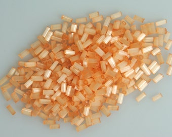 May include: A pile of small, translucent orange glass beads. The beads are cylindrical in shape and have a slightly iridescent finish.