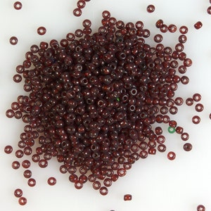 May include: A large pile of small, round, dark red glass beads with a few scattered around the pile.