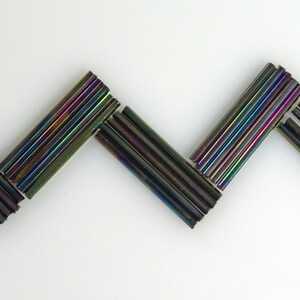 May include: A zig-zag pattern made of iridescent black glass rods.