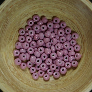 May include: A bowl filled with pink glass beads. The beads are round and have a white center.