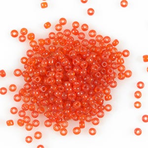 May include: A large pile of small, round, orange glass beads. The beads are scattered on a white surface.