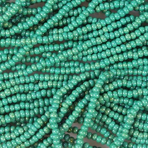 May include: A close-up of a large quantity of turquoise seed beads. The beads are small and round, and they are arranged in a random pattern.
