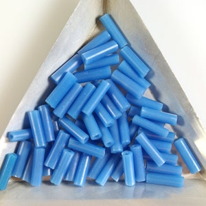 May include: A pile of small, light blue glass beads in a triangular metal tray. The beads are cylindrical in shape and have a smooth, glossy finish.