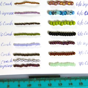 May include: A close-up of a white surface with rows of different colored beads. The beads are arranged in pairs, with each pair labeled with a size and type of bead. The sizes range from 6/0 to 15/0, and the types are Czech and Japanese.