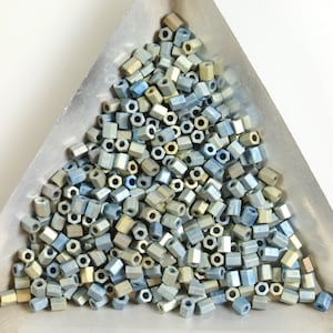 May include: A pile of small, hexagonal beads in shades of blue and gold. The beads are arranged in a triangular shape in a metal tray.