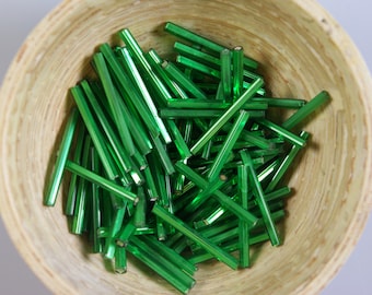 May include: A bowl filled with green glass beads. The beads are long and thin, and they are arranged in a random pattern.