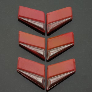 May include: Six red glass tiles with a silver trim. The tiles are shaped like a chevron or arrowhead.