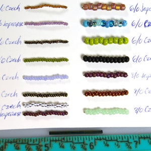 May include: A close-up of a white surface with rows of different colored beads. The beads are labeled with their size and type, including Czech and Japanese beads. The sizes range from 6/0 to 8/0. A ruler is visible at the bottom of the image.