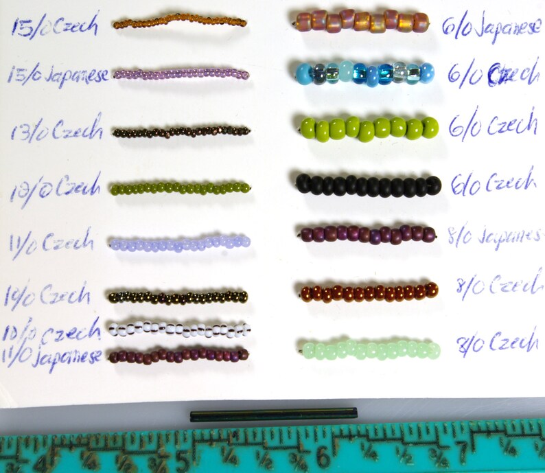 May include: A close-up of a white surface with rows of different colored beads. The beads are labeled with their size and type, including Czech and Japanese beads. The sizes range from 6/0 to 8/0. A ruler is visible at the bottom of the image.