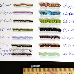 May include: A white card with rows of different colored beads. The beads are labeled with their size and type, such as 15/0 Czech, 6/0 Japanese, and 8/0 Czech. The card also includes a ruler for measuring the beads.