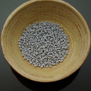 May include: A bowl filled with white and black striped glass beads. The beads are small and round, and they are arranged in a random pattern.
