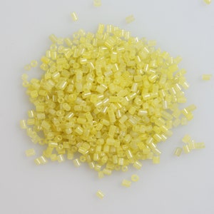 May include: A large pile of small, translucent yellow beads. The beads are cylindrical in shape and have a slightly frosted finish.