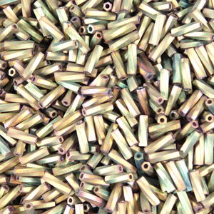 May include: A close-up shot of a pile of metallic, hexagonal beads. The beads have a gold and green iridescent finish. The beads are cylindrical with a hole running through the center. The beads are scattered randomly.