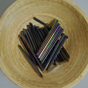 May include: A bowl filled with iridescent glass rods. The rods are approximately 1 inch in length and have a variety of colors, including purple, blue, green, and gold.