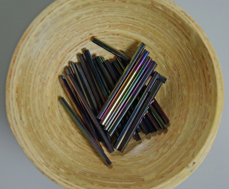 May include: A bowl filled with iridescent glass rods. The rods are approximately 1 inch in length and have a variety of colors, including purple, blue, green, and gold.