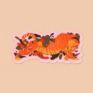 May include: A pink sticker featuring an orange and black tiger illustration. The tiger is curled up in a ball with its head resting on its paws. The background is a pink and white swirl pattern.