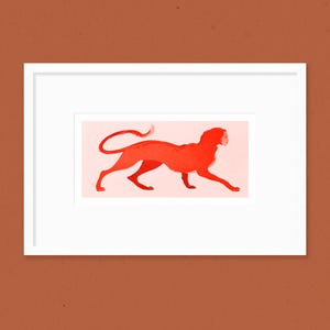 May include: A framed art print featuring a stylized illustration of a red creature with a woman's face, walking to the right. The artwork is set against a light pink background, with a white frame and a brown background.