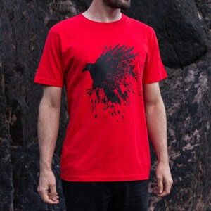May include: Red t-shirt with a black silhouette of a raven with splatter paint design. The raven has text on it that says "The flow is the way".