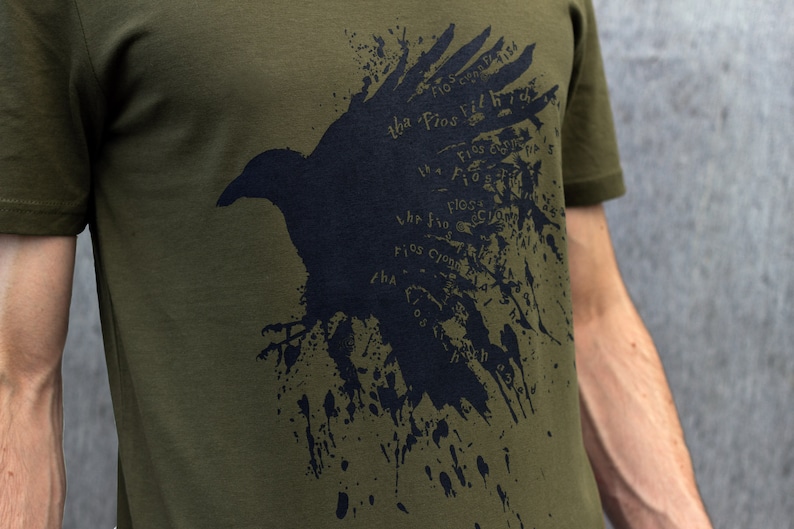 May include: A dark green t-shirt with a black crow graphic. The crow is made up of the words "The Fios Did Fly High" repeated in a splatter pattern.