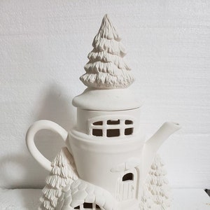 May include: White ceramic teapot shaped like a house with a tree on top. The house has a door, windows, and a stone-like base. The teapot is ready to be painted.