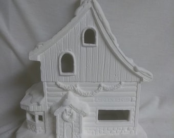 May include: White ceramic Christmas village house with a snow-covered roof, a wreath on the door, and a sign that reads "Workshop".