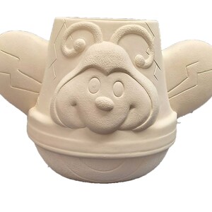 May include: A white ceramic planter shaped like a bee with a smiling face and large wings. The planter is ready to be painted.