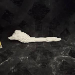 May include: A white ceramic pipe with a detailed, textured design. The pipe features a stylized animal head at one end and a long, textured stem. The object is set against a dark, patterned background.