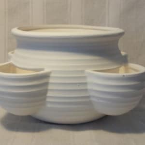May include: White ceramic planter with four separate planting areas. The planter has a rounded, bowl-like shape with a raised rim and a textured, ribbed surface.