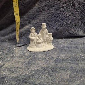 May include: White ceramic figurine of a family of four walking together. The family is dressed in winter clothing and the father is wearing a top hat.