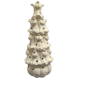 May include: A white ceramic Halloween tree-shaped decoration. The tree features cut-out star shapes and ghost-shaped faces. The tree is a stacked design with a rounded base.