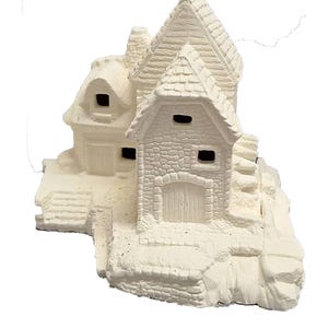 May include: White ceramic cottage with a stone-like texture, featuring a gabled roof, windows, and a door. The cottage is set on a base with steps leading up to the entrance.