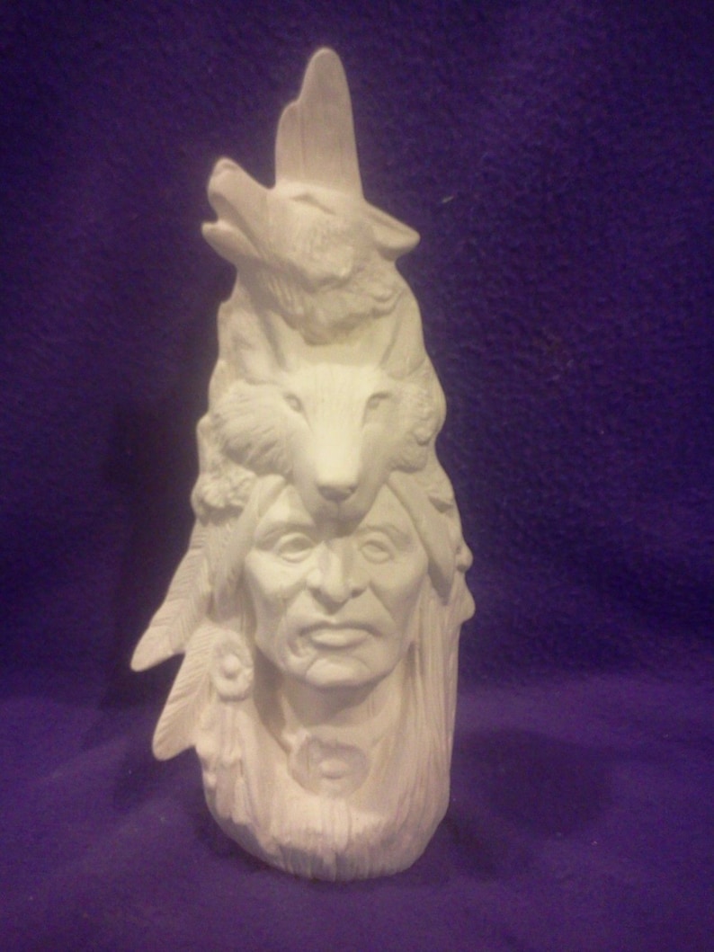 May include: White ceramic figurine of a Native American man with a wolf headdress. The man has a serious expression and is wearing a feathered headdress. The wolf is howling and has a detailed face.