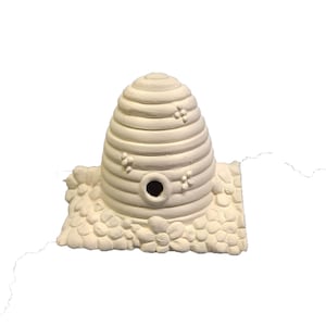 May include: A white ceramic beehive with a small hole in the front. The beehive is sitting on a base with a flower design.