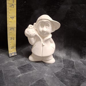 May include: White ceramic figurine of a boy wearing a hat and holding a small animal. The figurine is standing on a black surface.