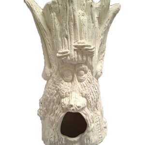 May include: White ceramic tree trunk sculpture with a face and a hollow opening. The sculpture is designed to look like a tree with a face carved into it.