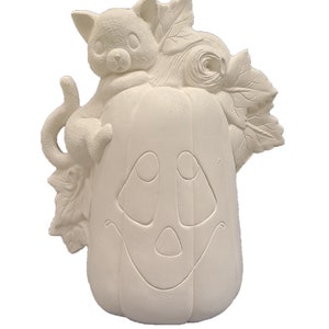 May include: White ceramic pumpkin with a smiling face and a small white cat sitting on top. The pumpkin has leaves and vines around it.