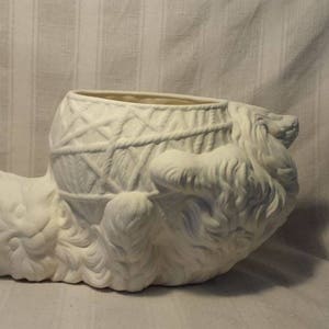 May include: White ceramic planter shaped like a cat's head with a basket on top. The planter is unpainted and ready to be decorated.