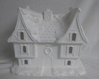 May include: White ceramic house with a snow-covered roof, a wreath on the door, and windows. The house is a blank canvas for painting and decorating.