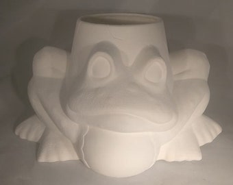 Può includere: Vaso da fiori in ceramica bianca a forma di rana con un'ampia apertura in cima per la semina. La rana è seduta con le gambe incrociate e ha un ampio sorriso con i denti.