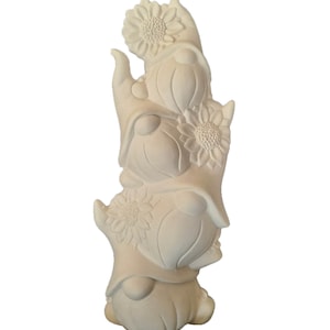 May include: A stack of three white ceramic gnomes, each with a sunflower on their hat. The gnomes are stacked on top of each other, with the top gnome holding the sunflower up high.